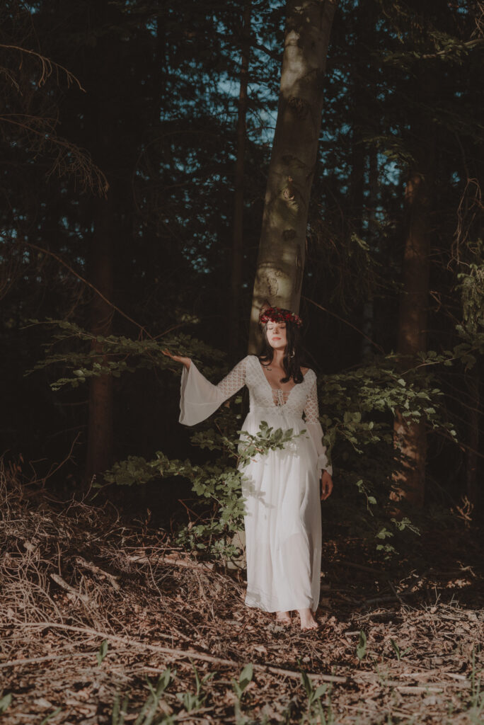 astrolog/tarocistka w białej sukni, z wiankiem z czerwonych kwiatów w lesie
