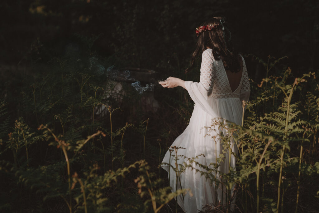 astrolog/tarocistka w białej sukni, z wiankiem z czerwonych kwiatów w lesie