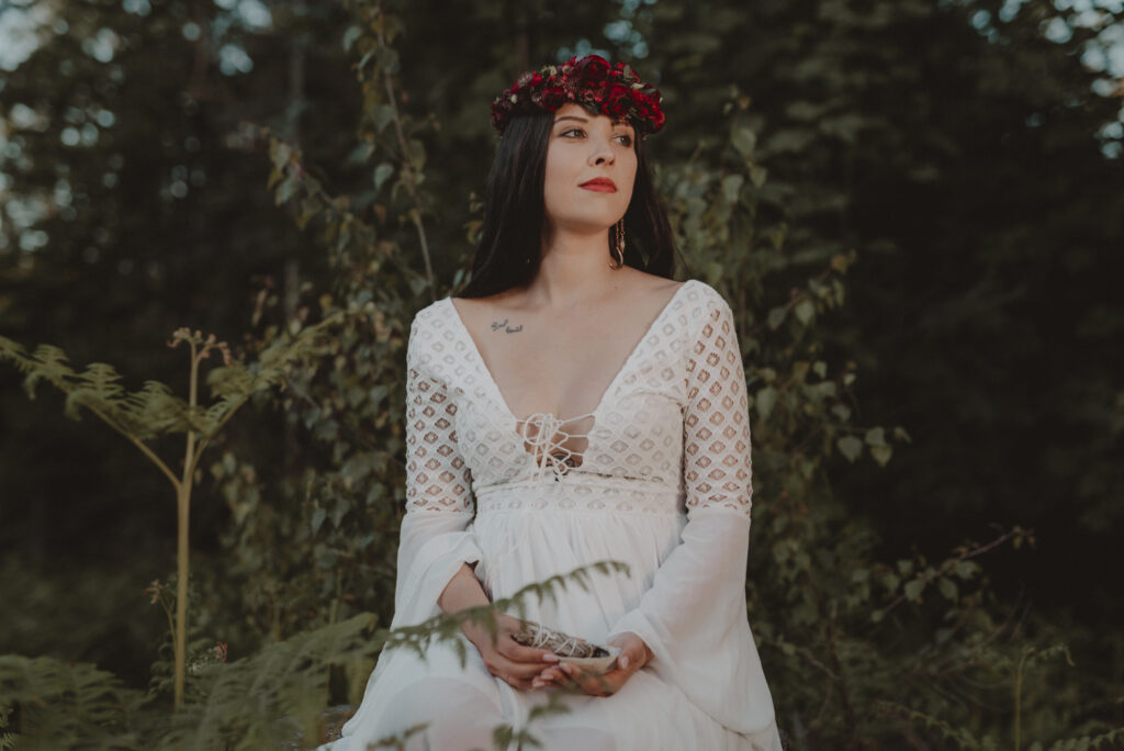 astrolog/tarocistka w białej sukni, z wiankiem z czerwonych kwiatów w lesie