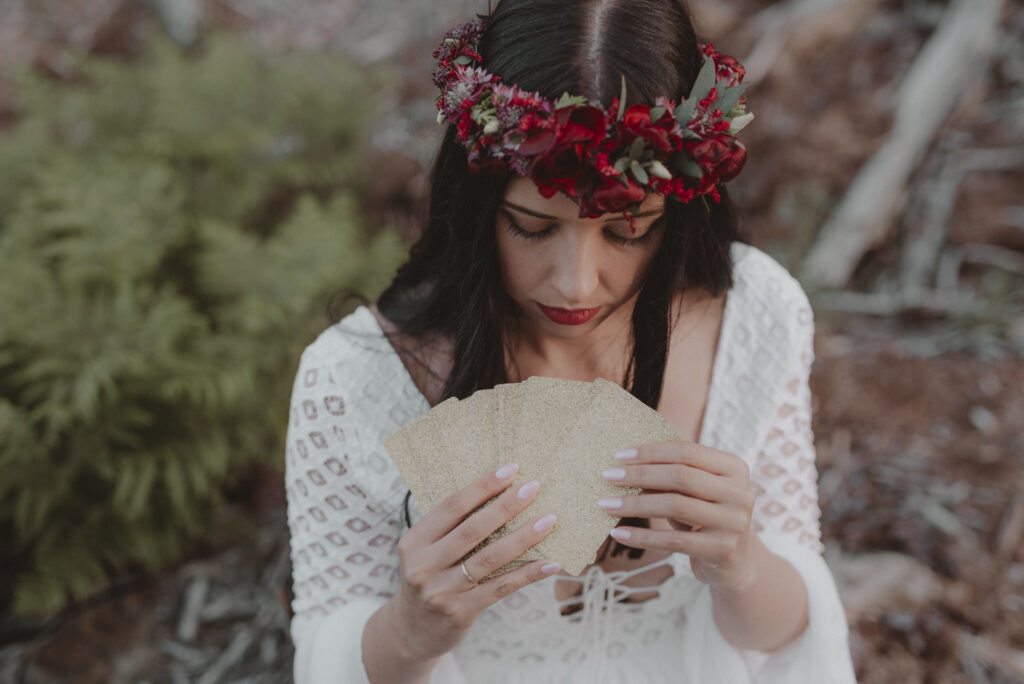 astrolog/tarocistka w białej sukni, z wiankiem z czerwonych kwiatów w lesie