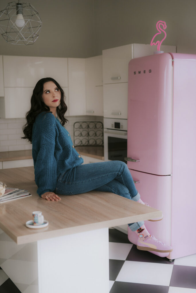 Autorka podcastu Astrokultura siedząca w kuchni na tle różowej lodówki smeg