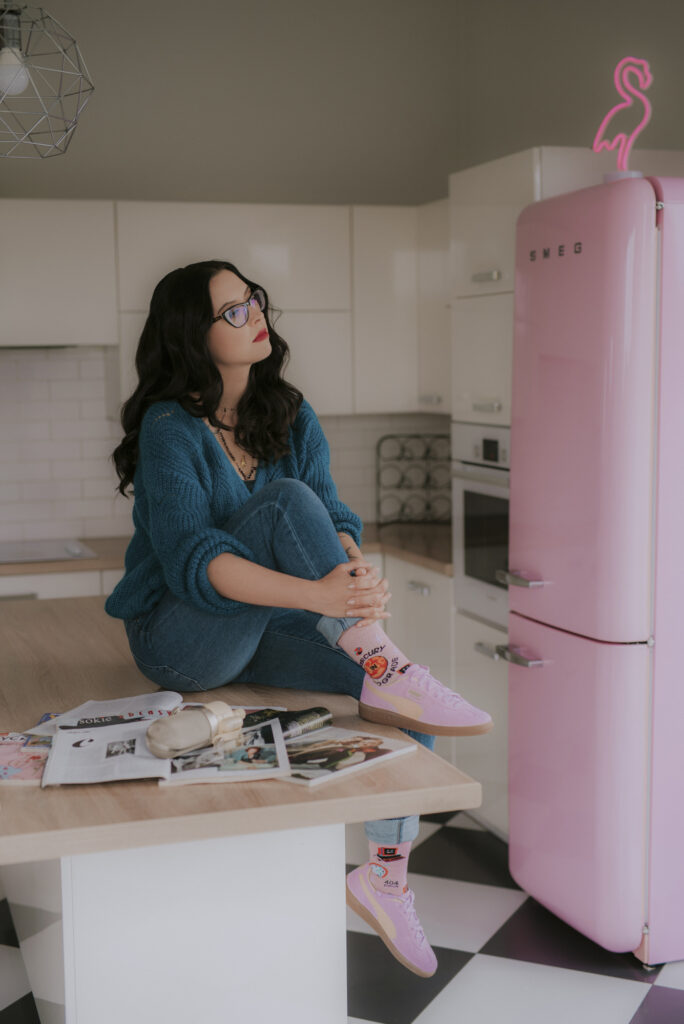 Autorka podcastu Astrokultura siedząca w kuchni na tle różowej lodówki smeg