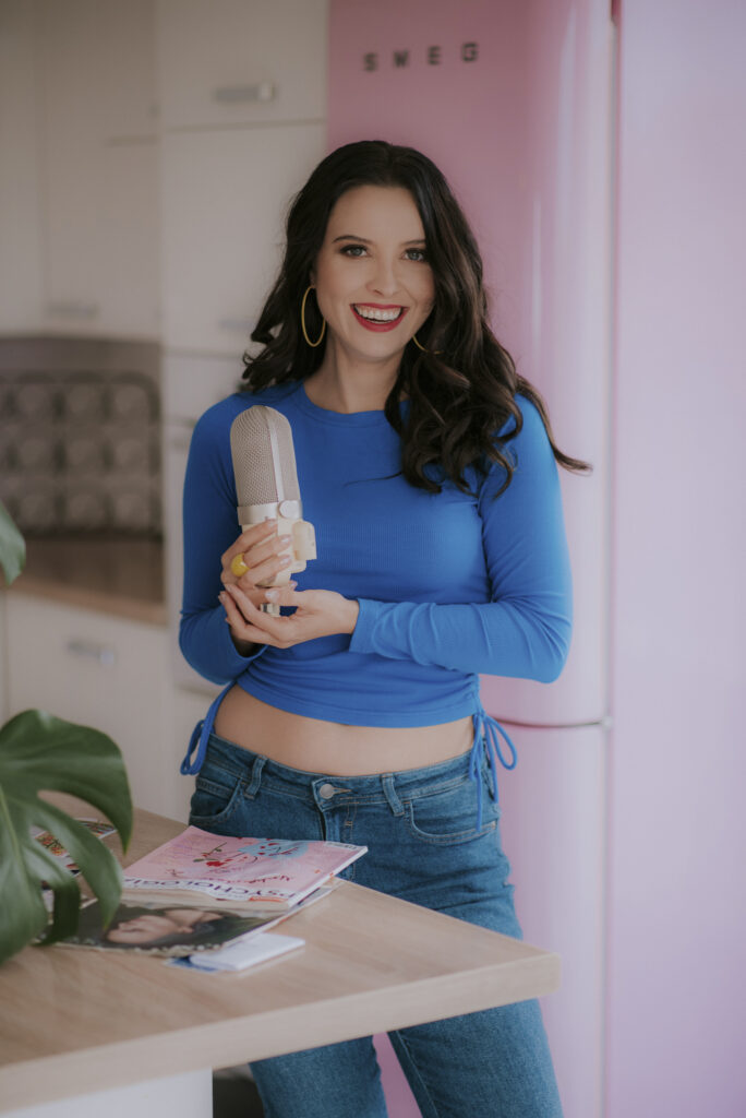 Uśmiechnięta astrolog Agata w niebieskim stroju z mikrofonem w dłoni - autorka Astrokultury