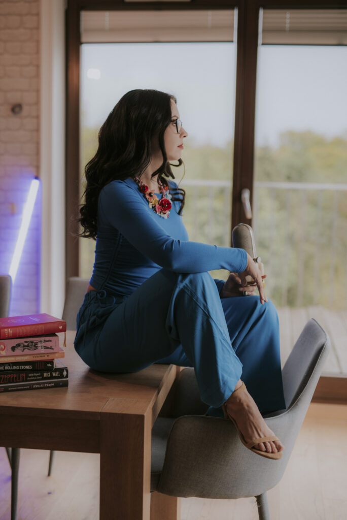 Astrolog Agata w niebieskim stroju siedząca na stole z książkami, z mikrofonem w dłoni - autorka Astrokultury