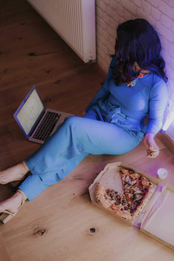Astrolog Agata w niebieskim stroju przy pracy z laptopem, jedząca pizzę - autorka Astrokultury
